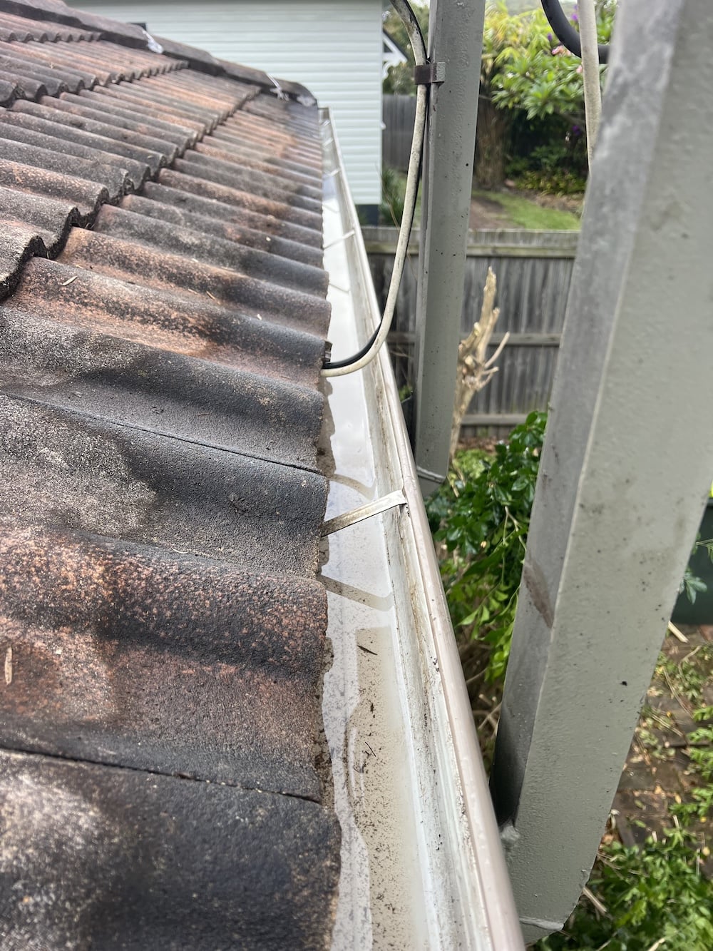 A close-up rooftop view of a freshly cleaned and cleared concrete tile roof gutter, completely free of weeds and dirt.